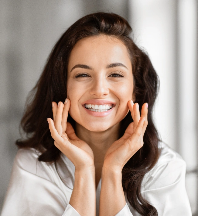 Smiling woman with hands near face in dental office setting, professional headshot.