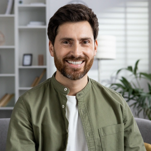Smiling man in green shirt at dental office, sitting in modern clinical setting with shelving.