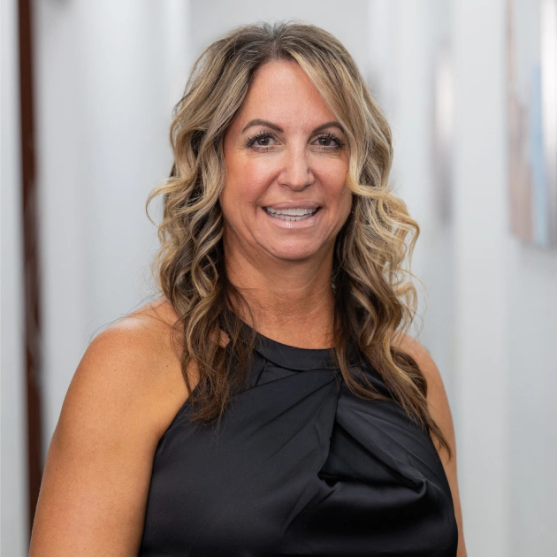 Professional woman in black shirt smiling at camera in modern dental office setting.